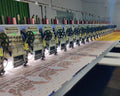 Row of embroidery machines in a factory setting with fabric and thread spools.