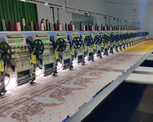 Row of embroidery machines in a factory setting with fabric and thread spools.