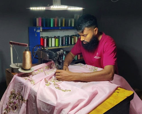 Man working on embroidery at a sewing machine with colorful spools of thread in the background.